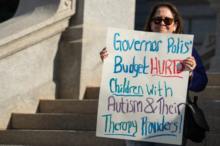 Robilyn Robison of Arvada, who has a 15-year-old child with autism, holds a sign criticizing Gov. Jared Polis’ proposed Medicaid budget cuts during a rally at the Colorado Capitol in Denver on Tuesday, Nov. 18, 2025.