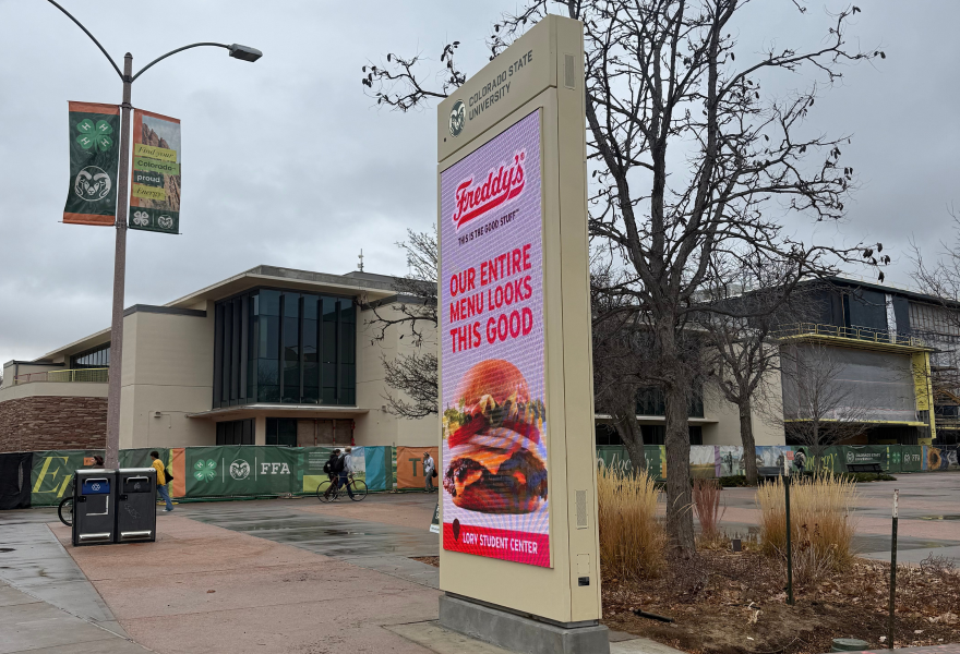 A digital sign shows a cheeseburger outside a larger building on a rainy day. 