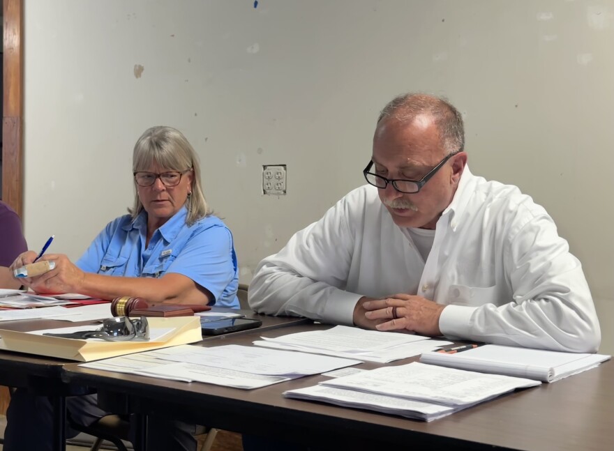 A man and woman sit at a table covered in papers