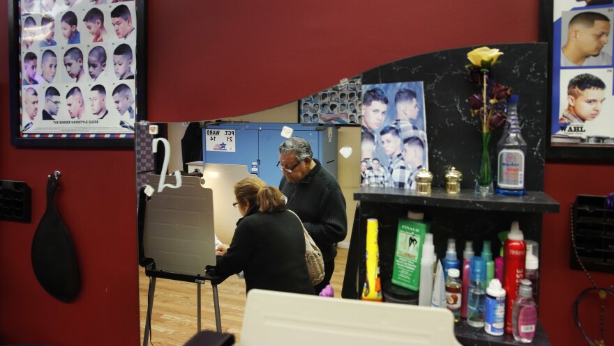 Democratic polling judge John Ramirez (right) is reflected in a mirror as he assists a voter filling out her ballot at Delia's Beauty Salon in Chicago on Tuesday.