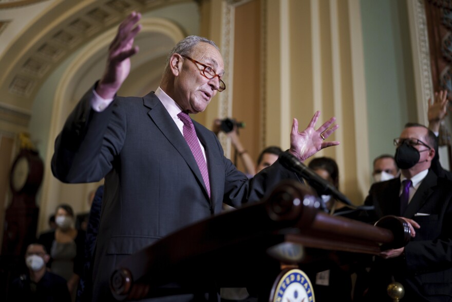 Senate Majority Leader Chuck Schumer, D-N.Y., holds up his arms standing behind a podium while talking to reporters at the U.S. Capitol on Tuesday.