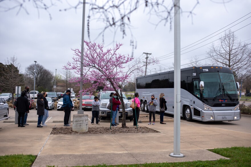 Dallas residents make a line outside of buses provided by the city. They wear masks and bundle up as they wait.  The buses are providing free rides to residents who need transportation to the COVID-19 vaccination appointment. 