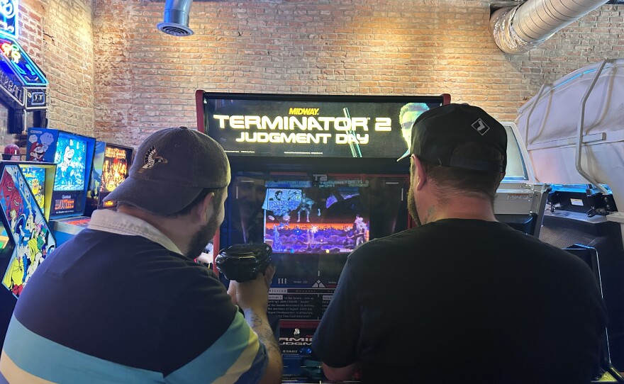 A view from behind two men playing the Terminator 2 arcade game