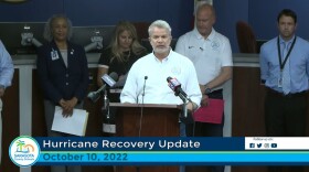 A screenshot of superintendent Brennan Asplen in a white button down shirt speaking at a podium