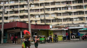 A woman and a child cross a street, with a residential high rise behind them. 