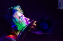 A man is squatting while starring into a screen, while red blue and green lights shine brightly into his face and neck.