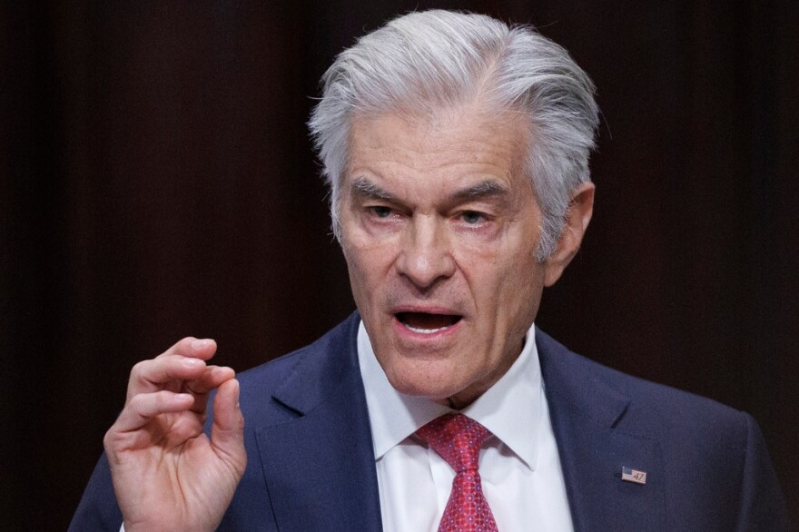 Man with gray hair wearing a blue suit and talking, looking to the left and gesturing with his right hand