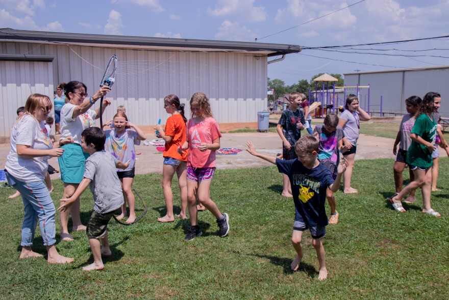  Teachers trade off holding a sprinkler while fourth grade students run and dance at Macomb Elementary School.