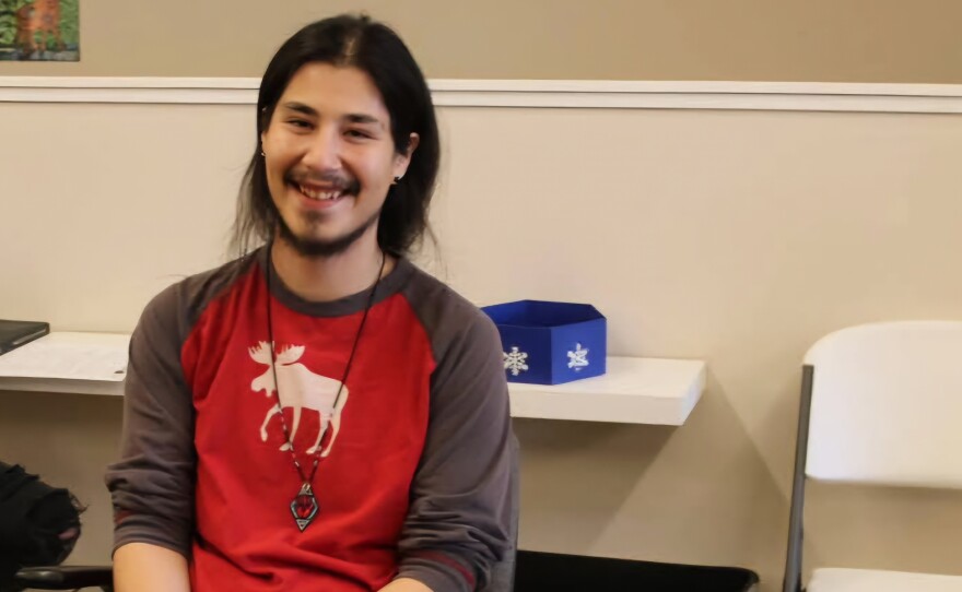 A person wearing a red long sleeved shirt near a table with a tan wall in the background