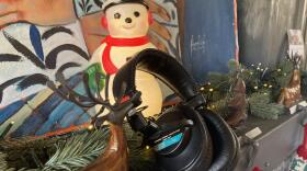 headphones rests on a holiday-decorated mantle with garland, wooden reindeer figurines, string lights, and a snowman decoration in the background.