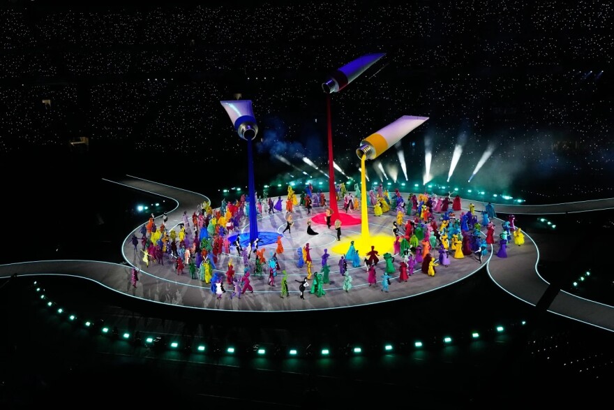 Giant tubes of paint hover over a stage as colorful characters dance below.