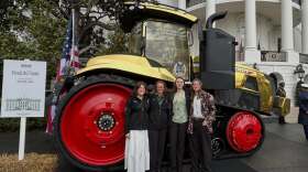 Four women standing in front of a gold-painted tractor in front of the Whitehouse.