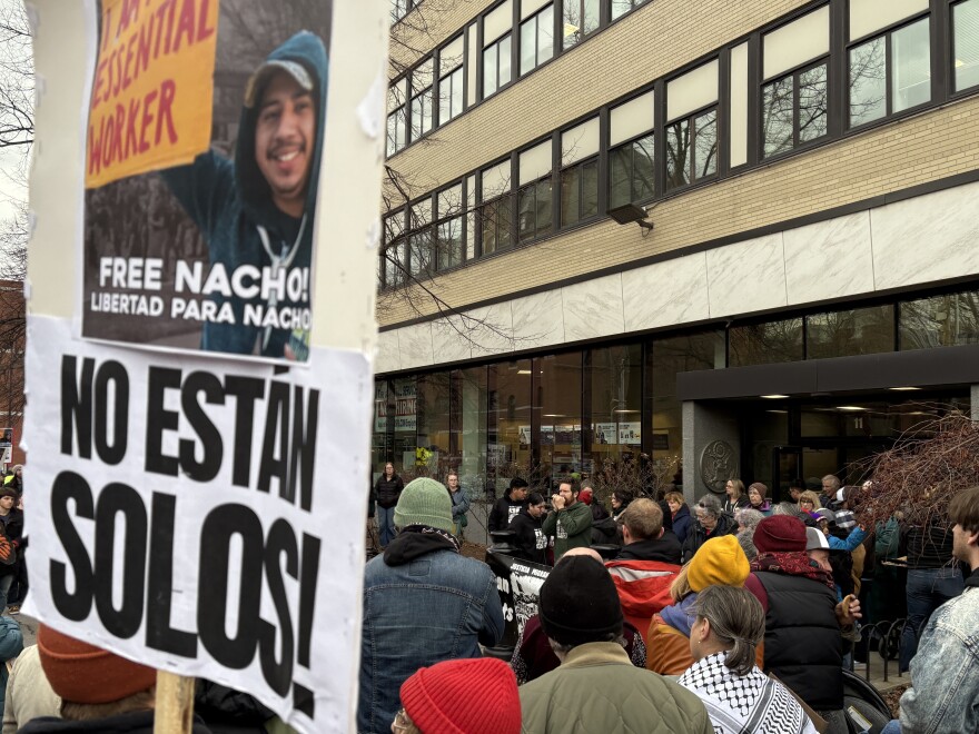 People gather outside a building. In the foreground is a sign that reads  "Free Nacho! and No estan solos!"