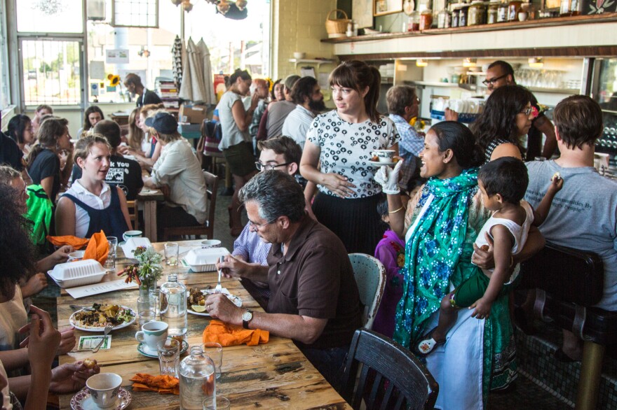 Minara Begum (foreground, far right), holds her daughter Laki while talking to customers at the first Bandhu Gardens pop-up dinner at Rose's Fine Food, a women-owned diner in Detroit, in July 2016.