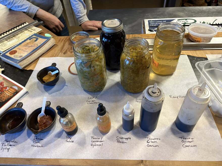 several bowls with sauces, and glass gars with fermented condiments, and squirt jars with sauces are labeled atop a counter for tasting.