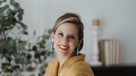 Soprano Emily Albrink sitting on the arm of chair wearing a yellow dress