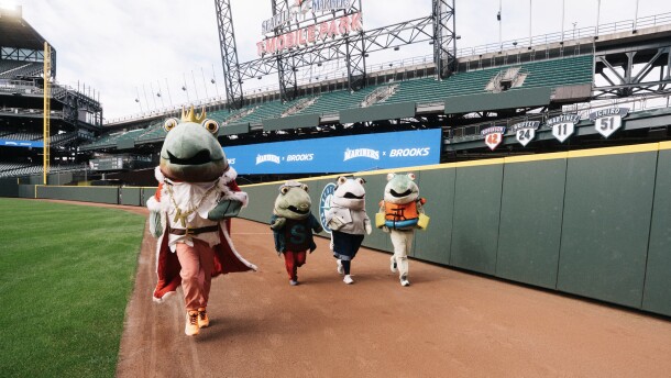 Four people dressed in salmon costumes run on a baseball field