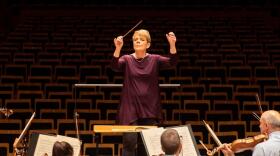 Conductor Marin Alsop with arms raised in front of the orchestra