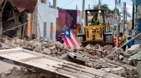 A Puerto Rican flag waves on top of a pile of rubble as debris is removed from a main road in Guanica, Puerto Rico on January 8, 2020, one day after the earthquake. (Ricardo Arduengo/AFP/Getty Images)
