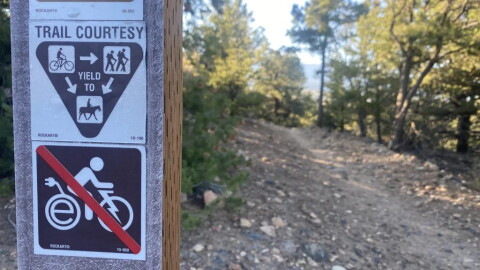 A courtesy trail marker reminds riders that e-bikes are not allowed on the trails outside of Salida. the top sign reads "Trail courtesy" with symbols indicating that bike riders must yield to pedestrians and horseback riders.