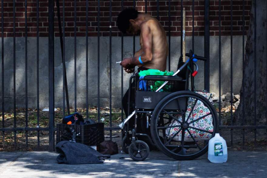 A man standing up from a wheelchair prepares to inject himself with a needle on Southampton Street in the Mass. and Cass area of Boston. (Jesse Costa/WBUR)