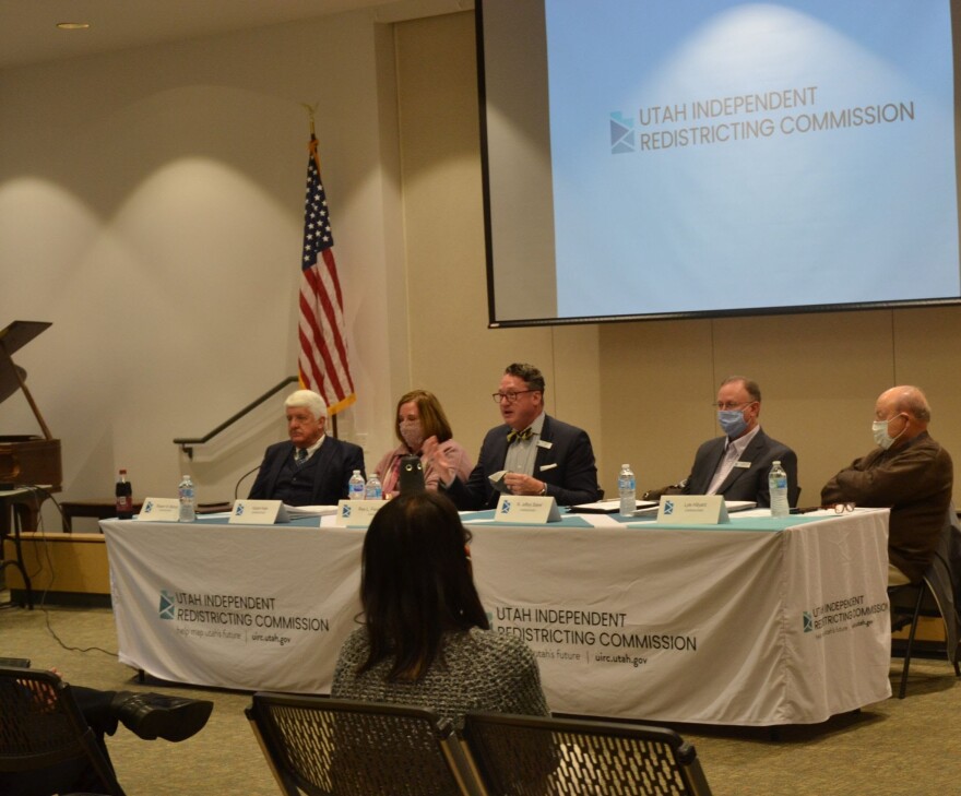 A photo of people sitting at a table with a tablecloth that reads 'Utah Independent Redistricting Commission.' 