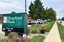 A Heartland Bank and Trust sign directs customers toward the ATM in front of a row of trees.