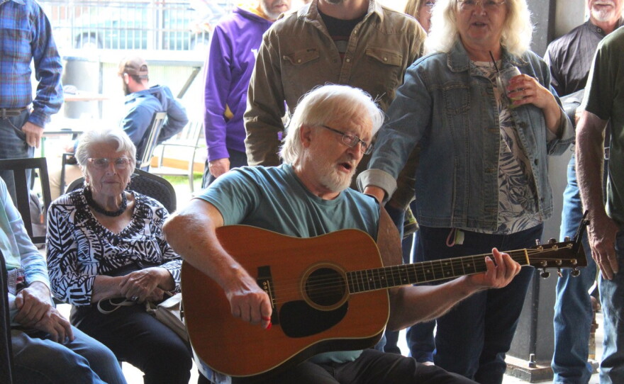 A man in the center plays his guitar with others surrounding him.