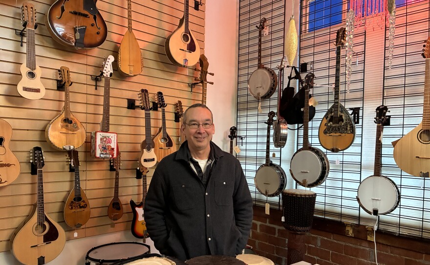 Eric Azumi stands in front of a wall of instruments at Lark in the Morning in Berkeley.