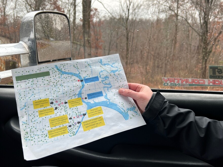 A hand holds a sheet of paper with a map of injection wells near Marietta. There are trees outside in the background.