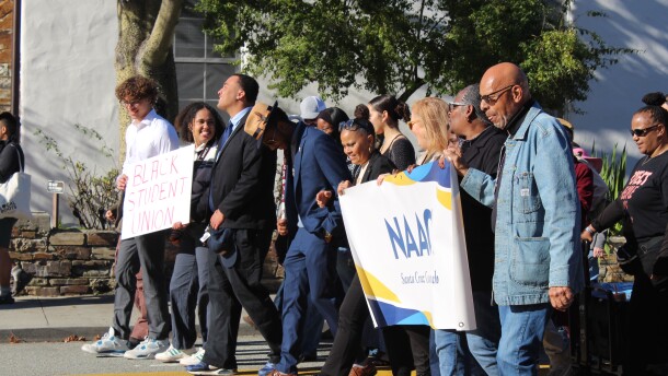 A line of people march together along a street. One sign reads "Black Student Union" and another reads "NAACP Santa Cruz County."