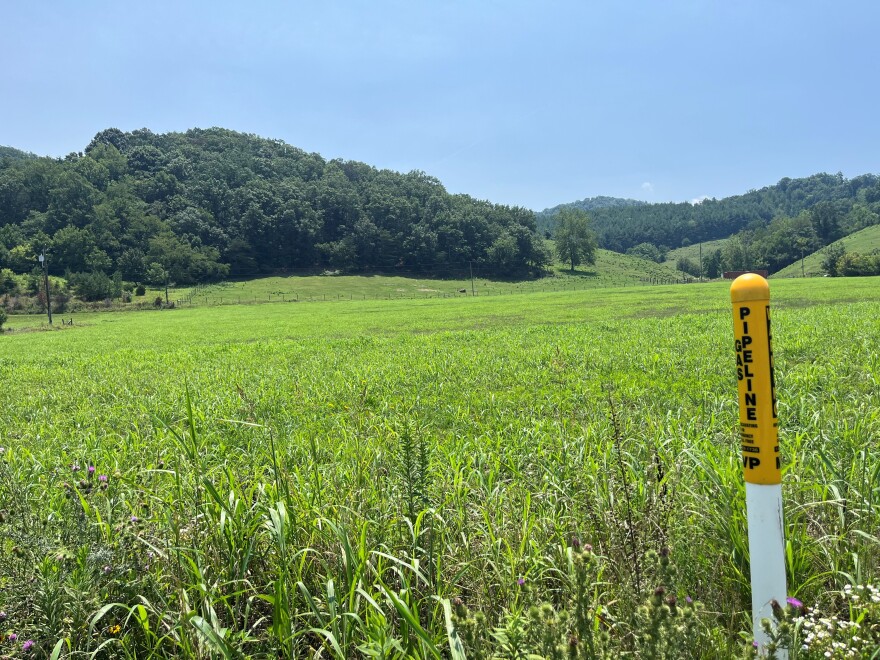 A field with rolling hills. In the foreground is a yellow pole that reads 'pipeline'.
