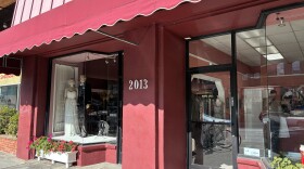 The facade of Uni Tailor in Downtown Berkeley is red. Two mannequins peak through the window, one in a white wedding dress and another in a suit.