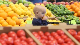 Ten-month-old Juni Riley enjoys a lemon while watching her mom, Lillian Riley, shop for fruit during the opening of the Whole Foods in Brighton on Wednesday, April 12, 2023.