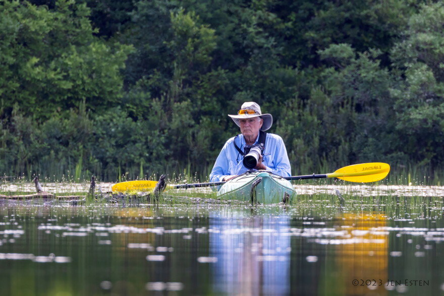 A man floats on a lake in a kayak with a camera.
