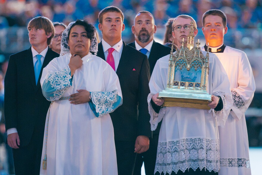 An attendant carries a reliquary containing a portion of the late Archbishop Fulton J. Sheen's jawbone as James Fulton Engstrom, in blue tie, and his brother process in during Sheen's beatification Mass on Thursday.