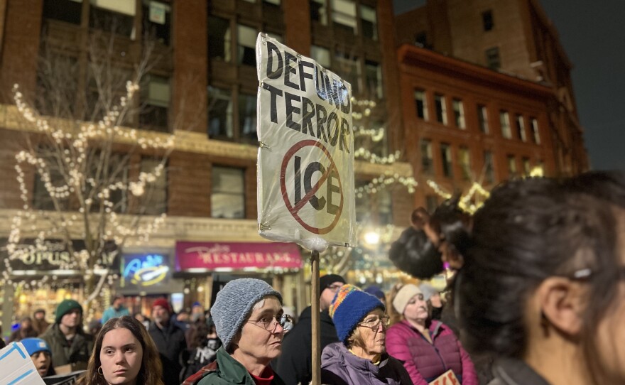 Protesters hold up signs and shout chants criticizing federal immigration enforcement activities.