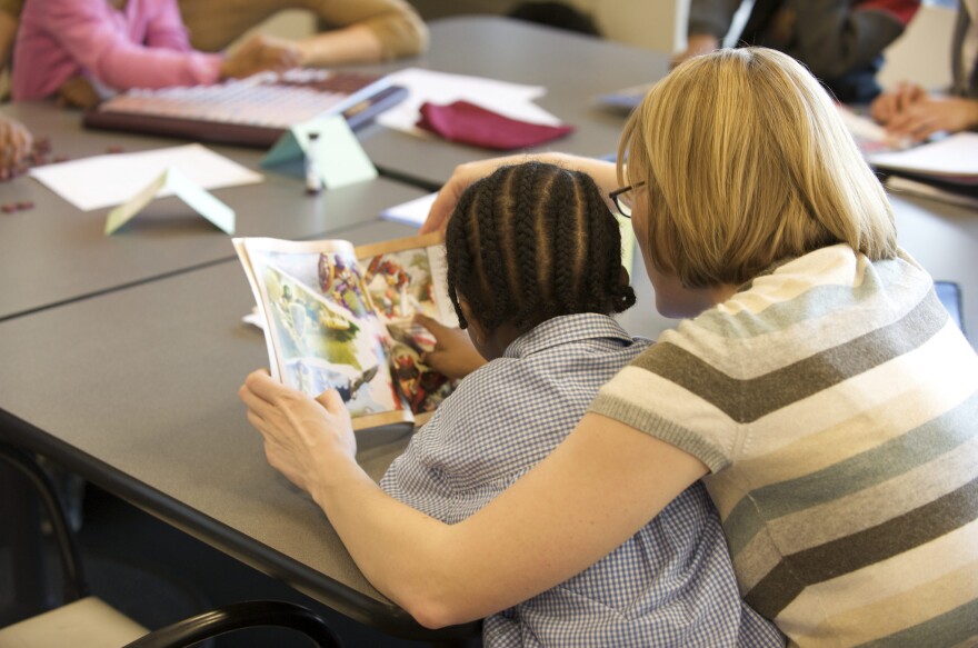 Teacher reading a book with a student.