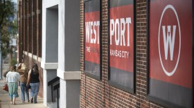 Exterior photo shows three people walking on a sidewalk away from the camera. A large brick building at right has a large painted sign that reads "Westport, the Original Kansas City."