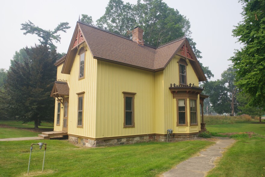 A yellow two story wood house stands on a green grass lawn. A thick blanket of fog looms around it. 