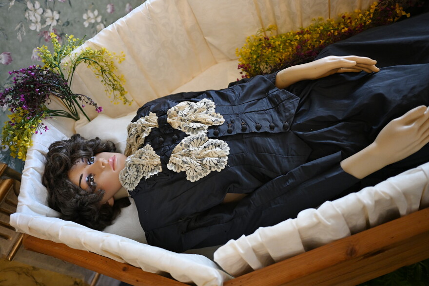 A mannequin lying in a coffin wearing a black dress with white lace