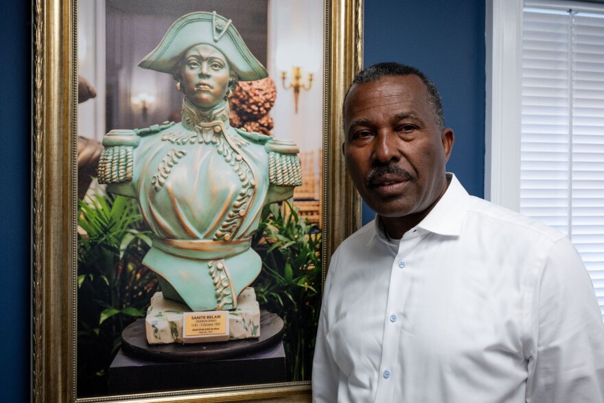 Norwalk Realtor Guy Bocicaut stands next to a photo featuring a bust of Haitian revolutionary leader Sanité Bélair at his offices in Norwalk on July 15, 2025. Bocicaut has called for a series of boycotts by immigrants and is seeking support from immigrant rights advocates.