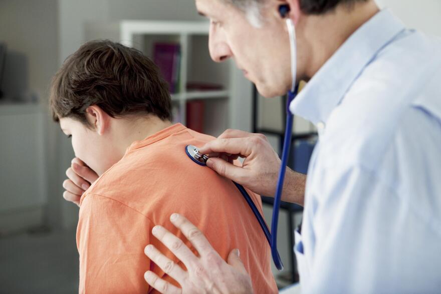 A doctor using a stethoscope on a young patient who is coughing
