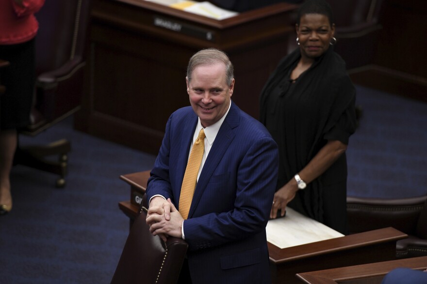 Man smiling in suit standing in front of a woman dressed in black