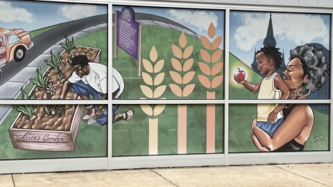 A mural on the outside of the Feeding America Eastern Wisconsin building in Milwaukee depicts a scene of a man tending to crops at the nearby Alice's Garden, and a woman carrying a child who's holding an apple