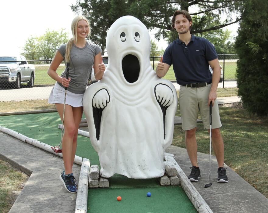 Two golfers posing next to a ghost statue