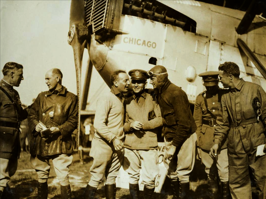 A sepia-colored picture with men wearing old military uniforms and regalia in front of a plane.