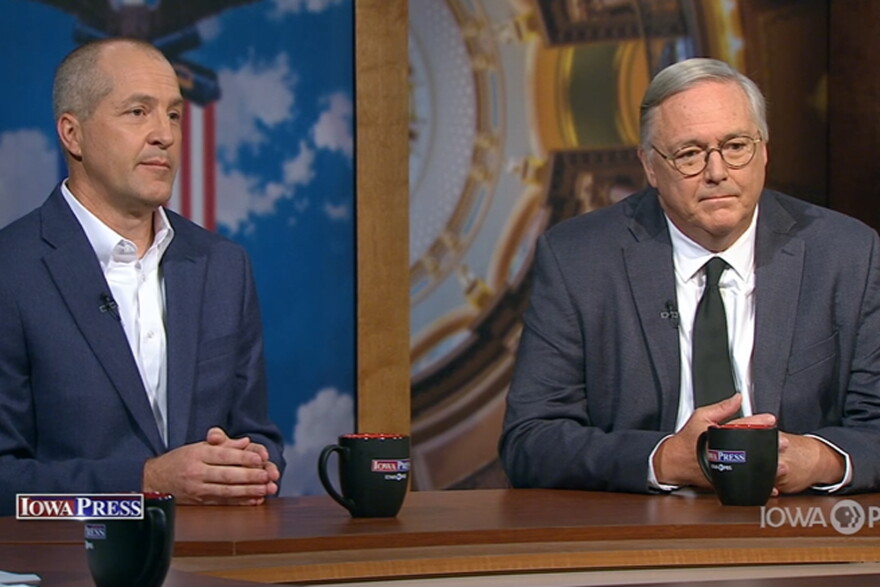Two men in suits sit a wood desk