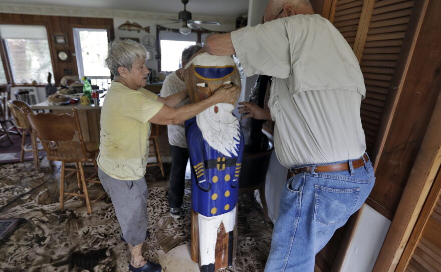 Bobbi Pattison, left, with help from her neighbors Hugh and Harriet Oglesby, stands up a sea captain statue carved out of wood from a 1993 storm at her home Friday, Sept. 2, 2016, in Steinhatchee, Fla. Hurricane Hermine was downgraded to a tropical storm after it made landfall, as it moves over Georgia, but the U.S. National Hurricane Center says winds are increasing along the Southeast coast and flooding rains continue. (AP Photo/Chris O'Meara)