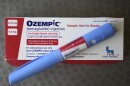 a blue pen-like injectable drug sits on top of a white and red box 